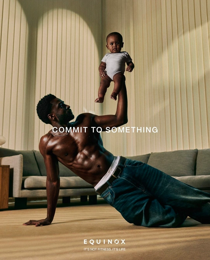 Father's Day creative ad: Shirtless father in a side plank lifting his baby overhead