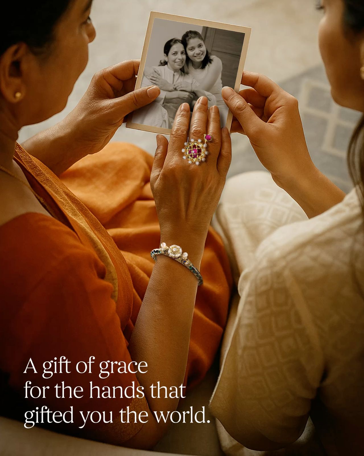 Mother and daughter's hands holding an old photo, with the mother wearing jewellery