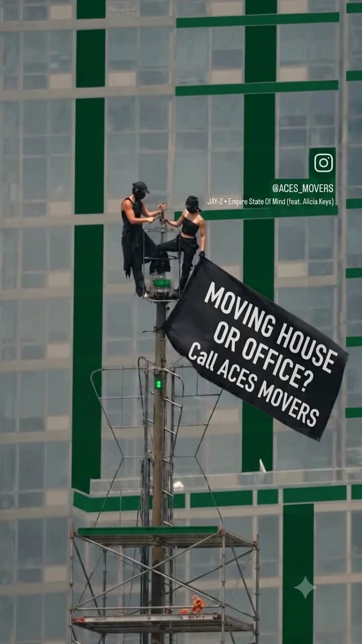 Movers & Packers creative ad: Workers hanging banner on scaffold, stunt-style ad