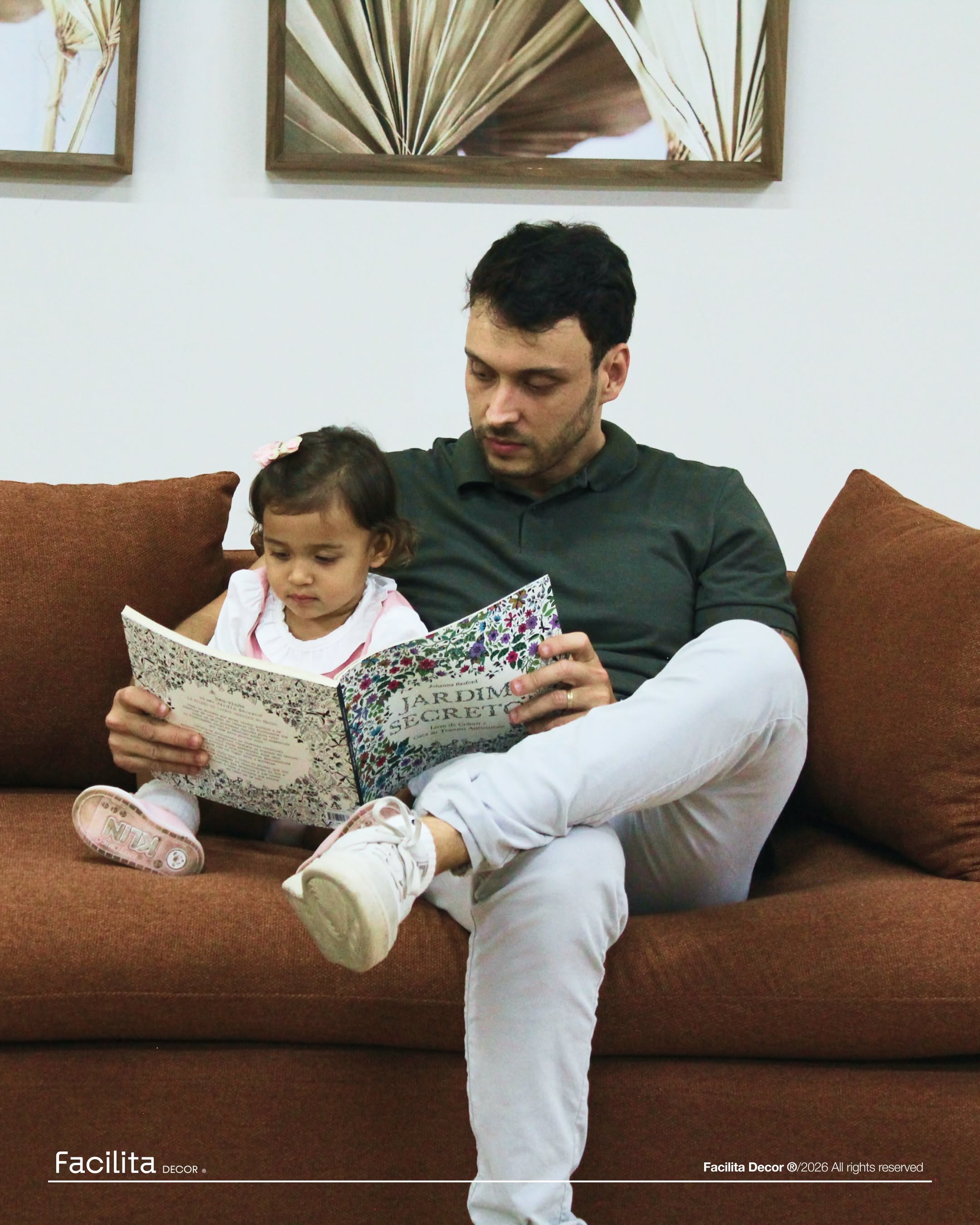Father lying on a rust sofa lifting his laughing baby daughter overhead