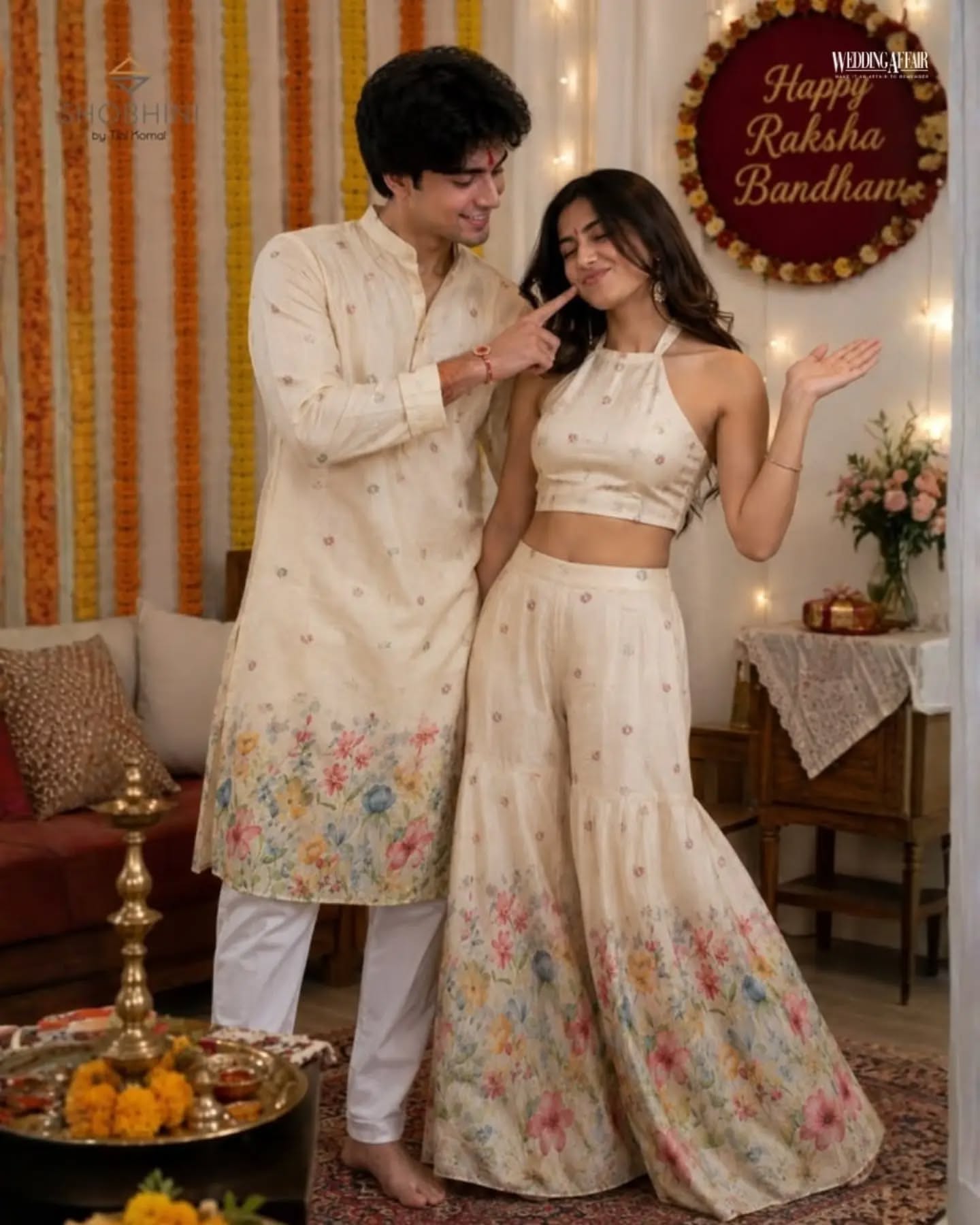Brother and sister in coordinated pastel ethnic outfits playfully tugging a wrapped gift on a sofa