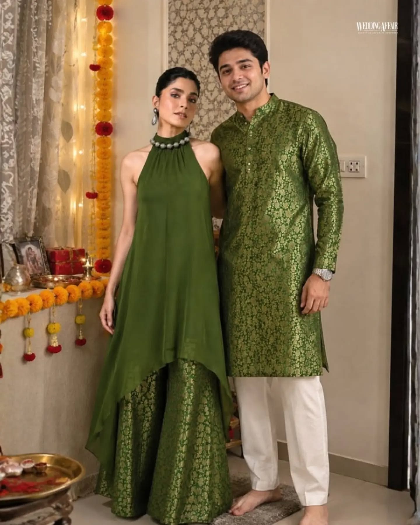 Brother and sister in coordinated pastel ethnic outfits playfully tugging a wrapped gift on a sofa