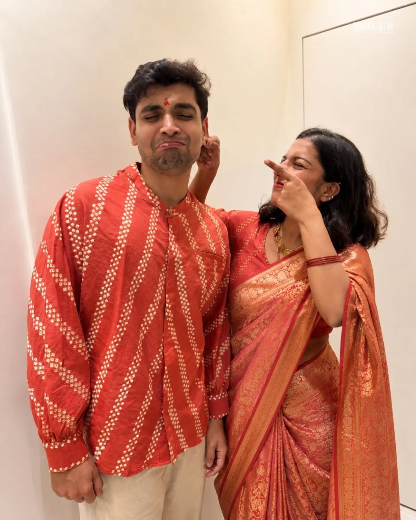 Brother and sister in coordinated pastel ethnic outfits playfully tugging a wrapped gift on a sofa