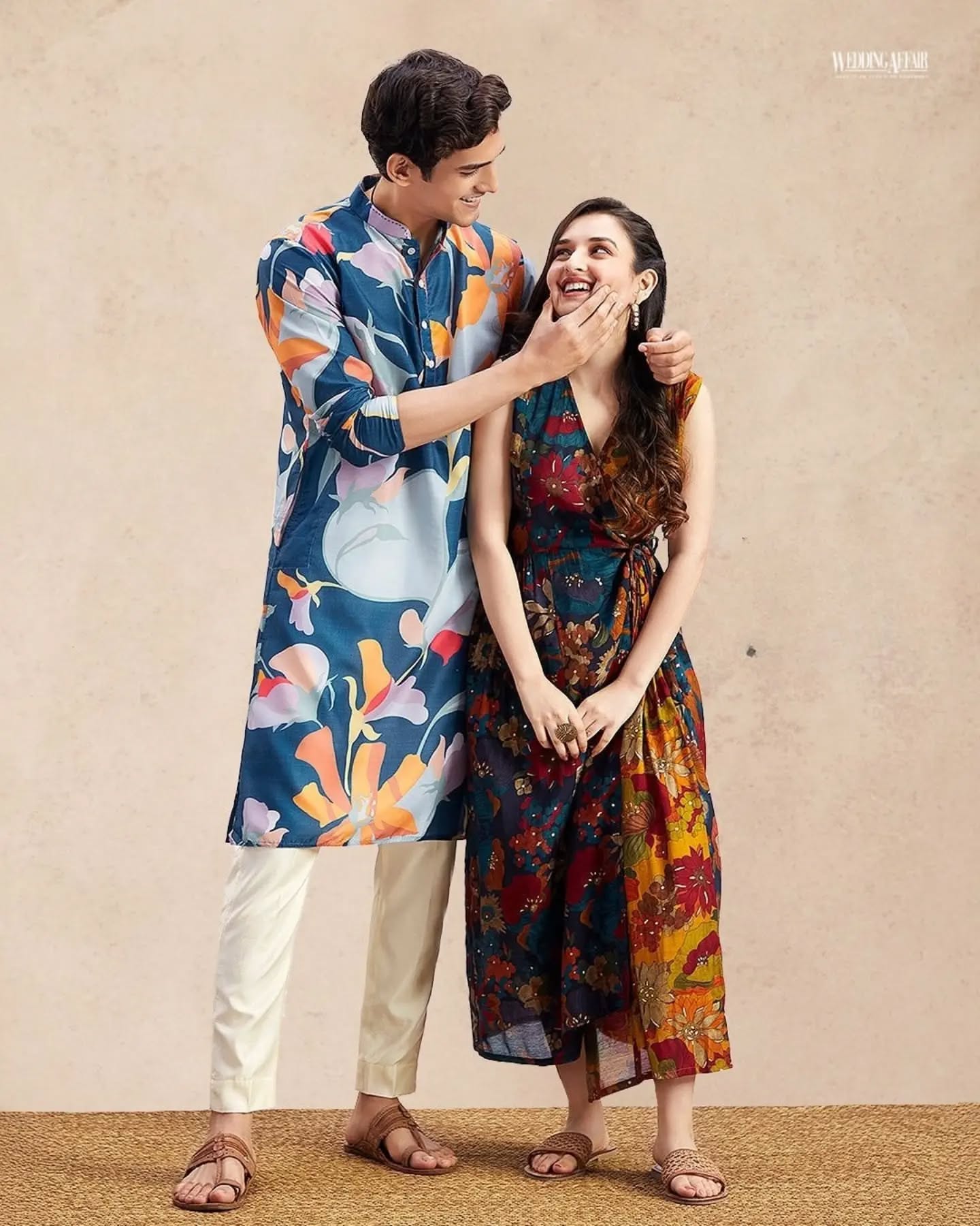 Brother and sister in coordinated pastel ethnic outfits playfully tugging a wrapped gift on a sofa