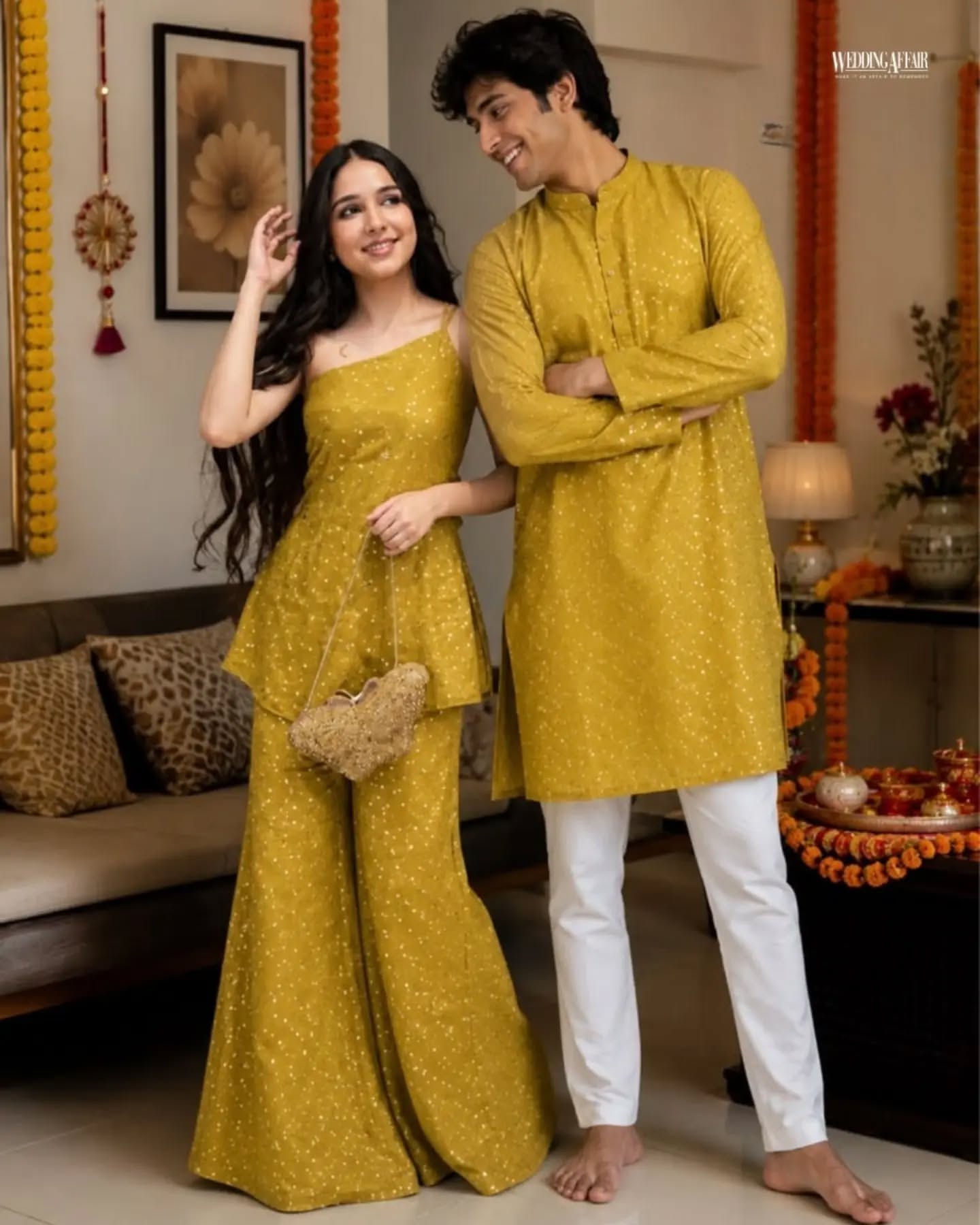 Brother and sister in coordinated pastel ethnic outfits playfully tugging a wrapped gift on a sofa