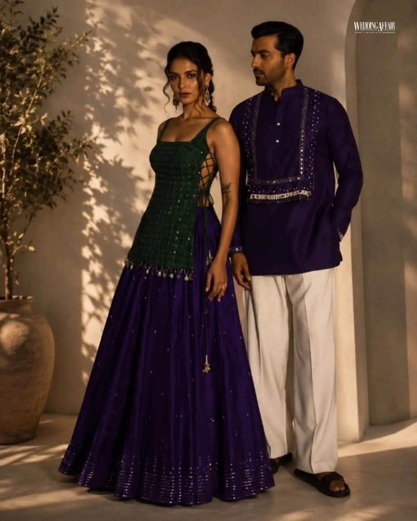 Brother and sister in coordinated pastel ethnic outfits playfully tugging a wrapped gift on a sofa