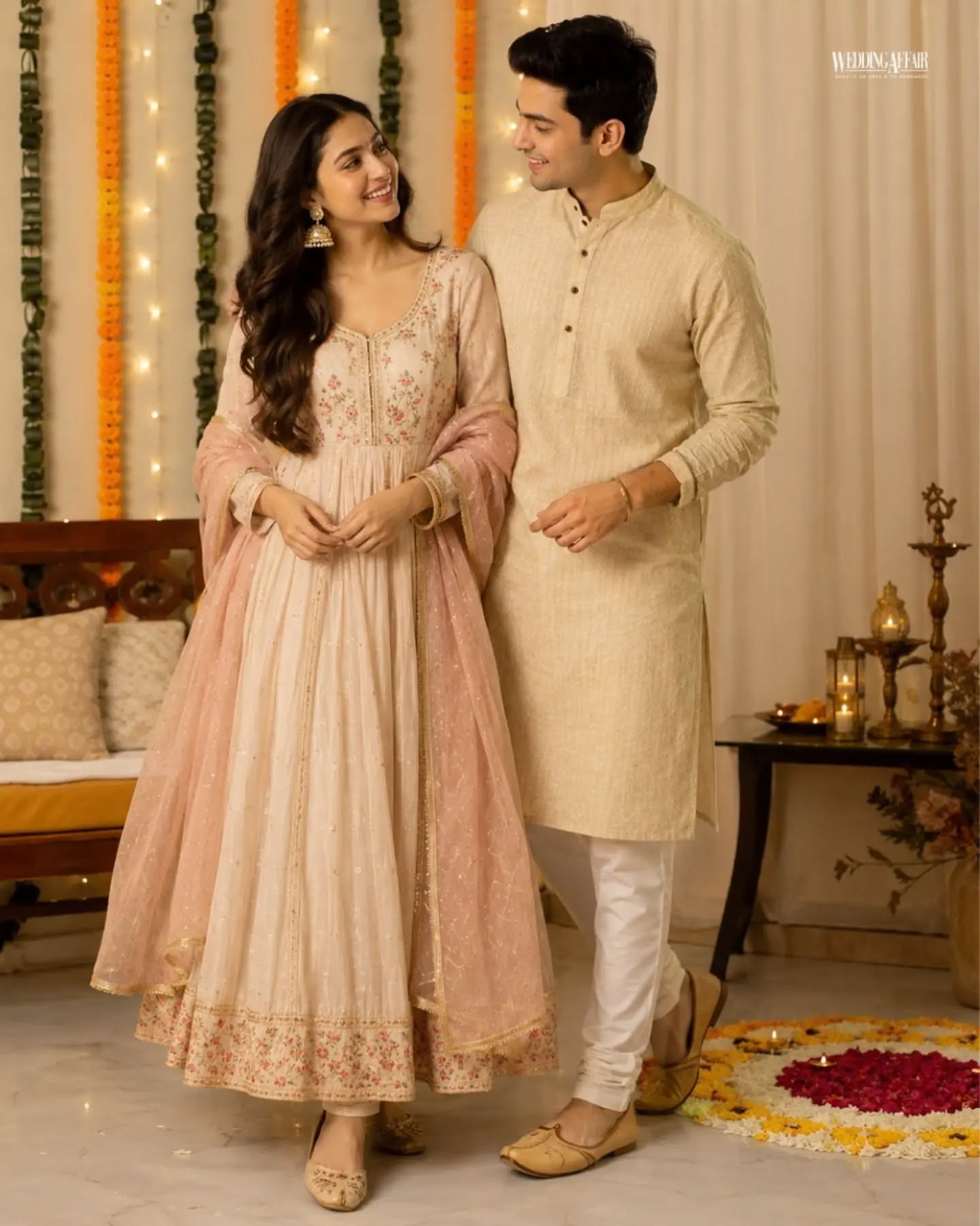 Brother and sister in coordinated pastel ethnic outfits playfully tugging a wrapped gift on a sofa