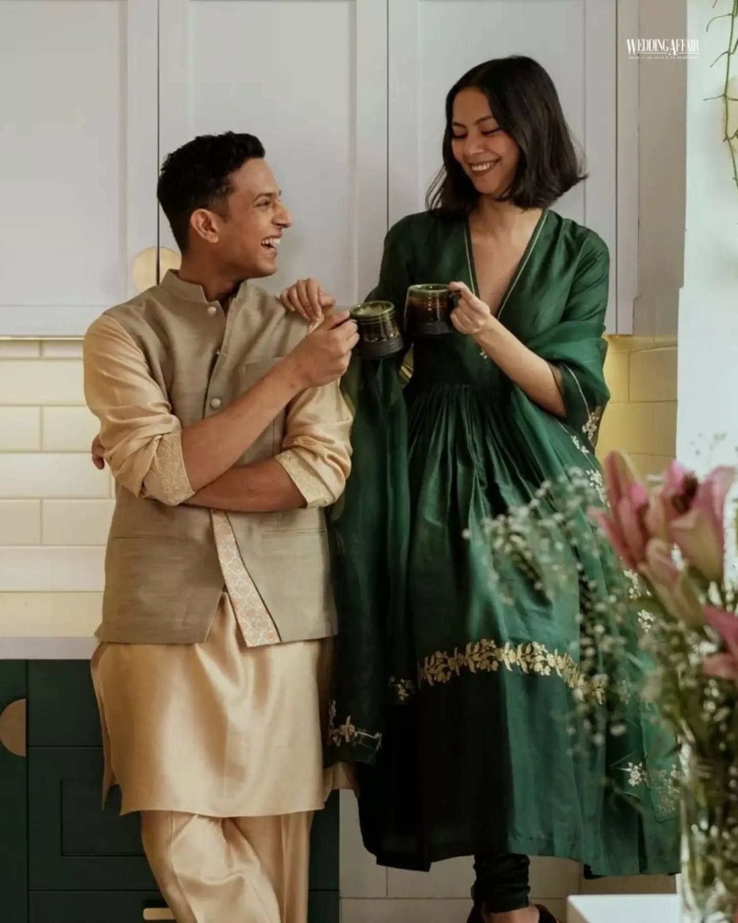 Brother and sister in coordinated pastel ethnic outfits playfully tugging a wrapped gift on a sofa