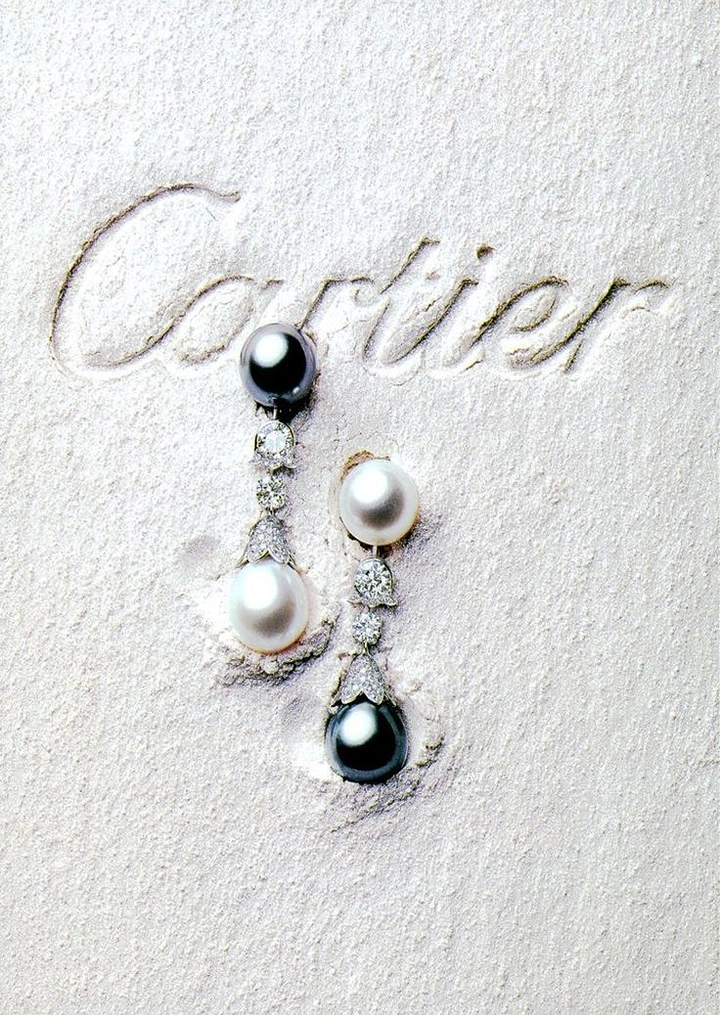 Jewellery creative ad: Pearl and diamond drop earrings pressed into white sand