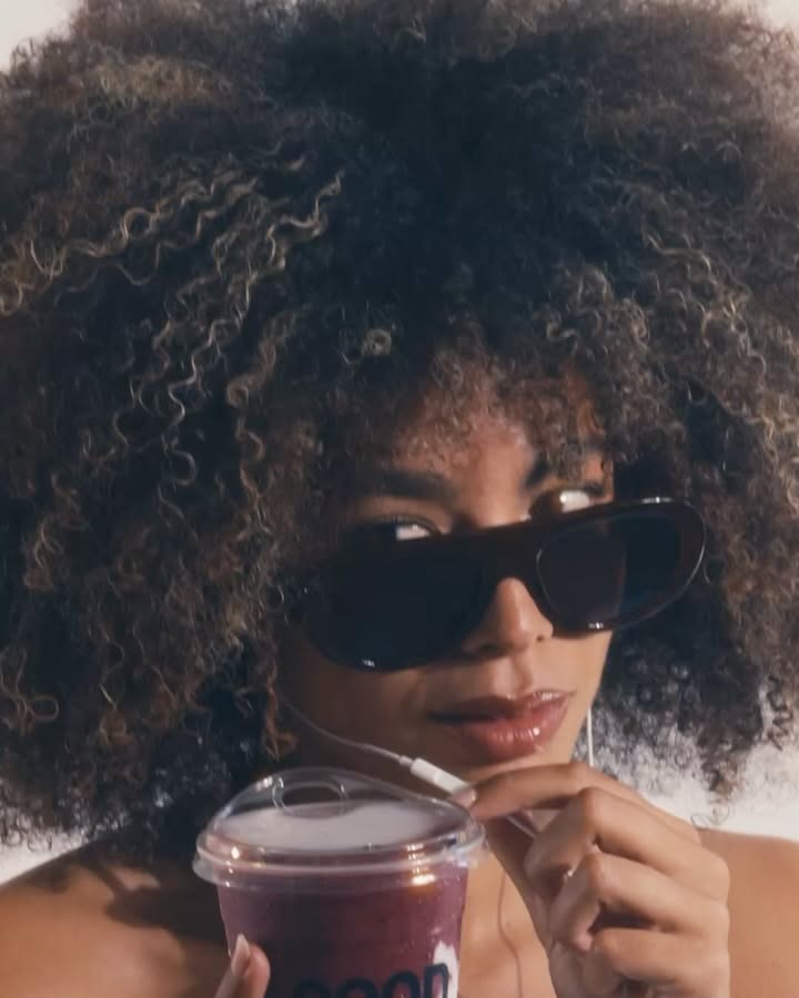 Carousel: Woman with voluminous curls in sunglasses holding a berry smoothie cup, slide 2