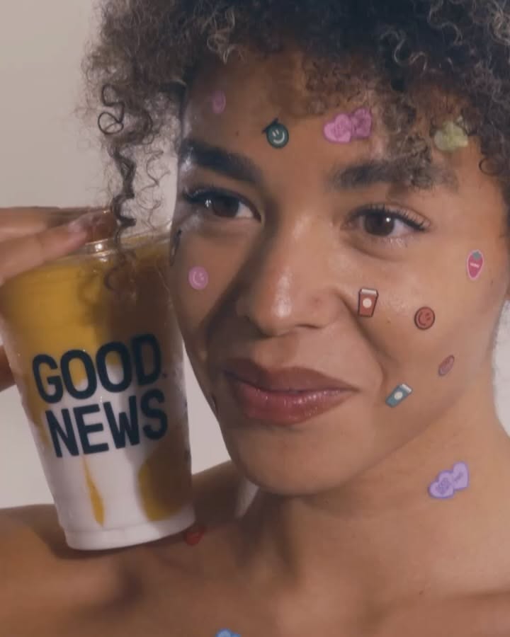 Carousel: Curly-haired woman with cute face stickers holding a mango smoothie cup, slide 2