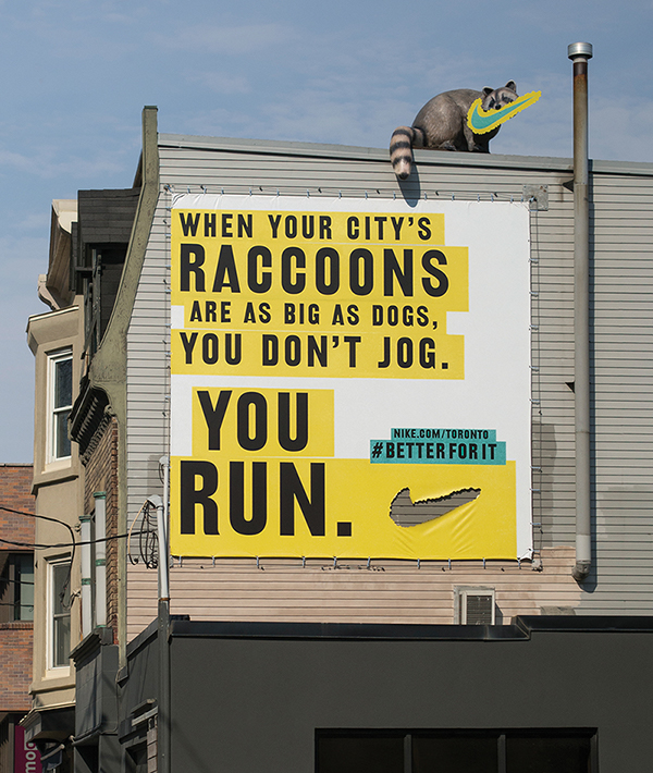 Poster: Rooftop billboard with a raccoon sculpture biting off the logo