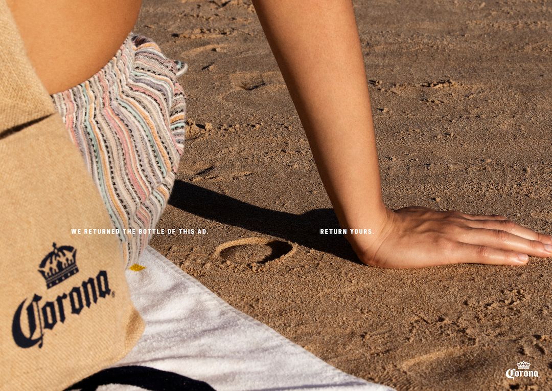 Circular bottle-base imprint in beach sand beside a sunbather's hand