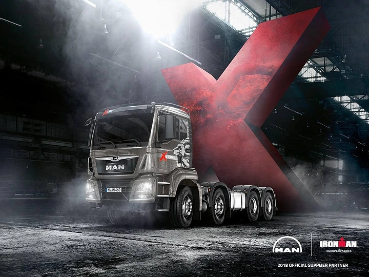 Automotive creative ad: Silver heavy truck in front of a giant red textured X in a smoky hangar