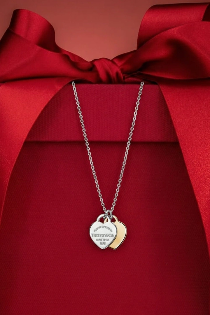Valentine's Day creative ad: Double heart tag necklace draped over a red gift box with a bow