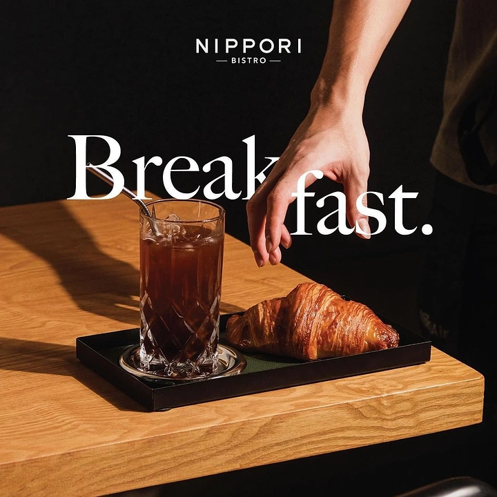 Coffee Shops creative ad: Croissant and iced coffee on a black tray with a hand reaching in