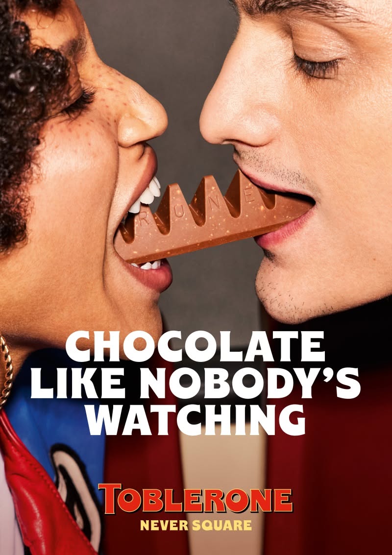 Two people biting opposite ends of a triangular chocolate bar