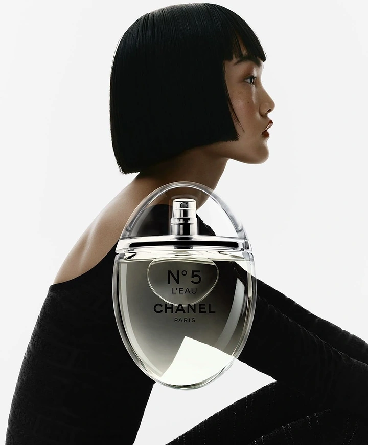 Creative ad: Profile of a model with a sharp black bob and an oversized clear perfume bottle