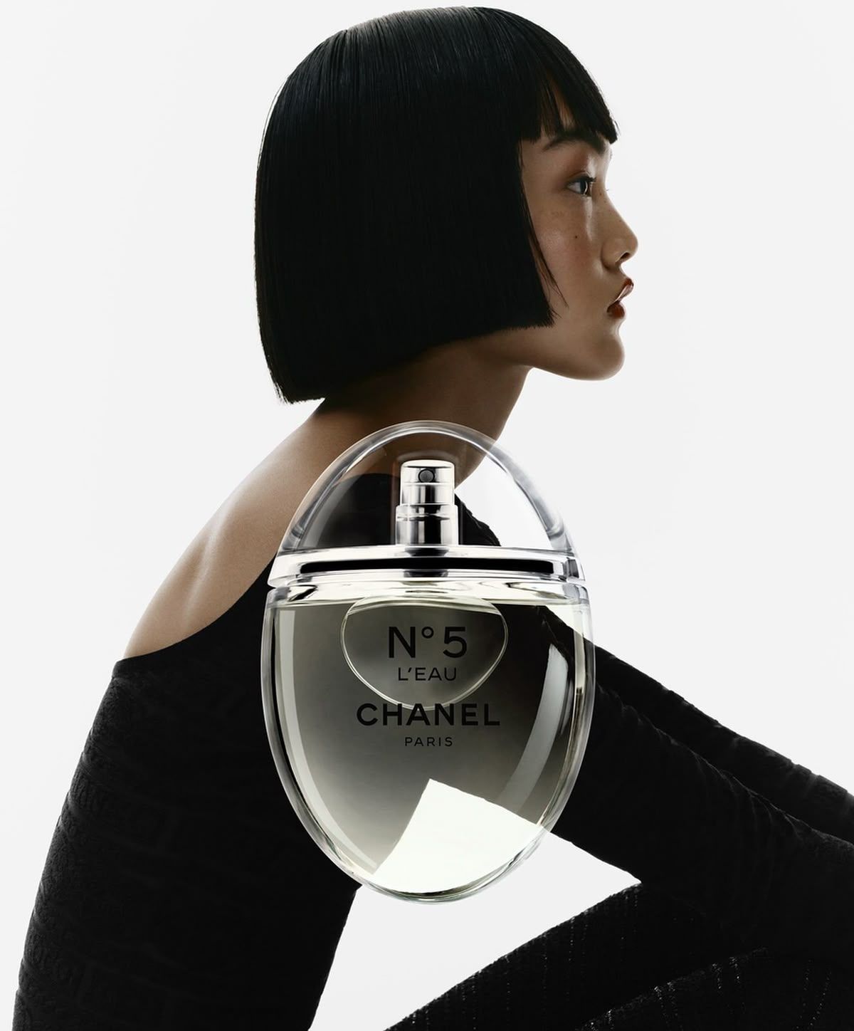 Instagram post: Profile of a model with a sharp black bob and an oversized clear perfume bottle
