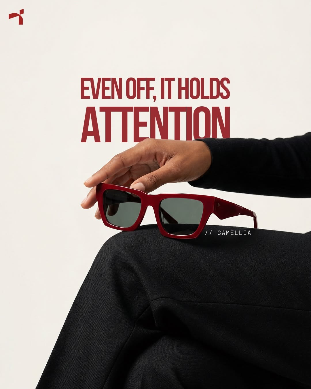 Carousel: Hand resting red acetate sunglasses on a knee in black trousers, slide 1