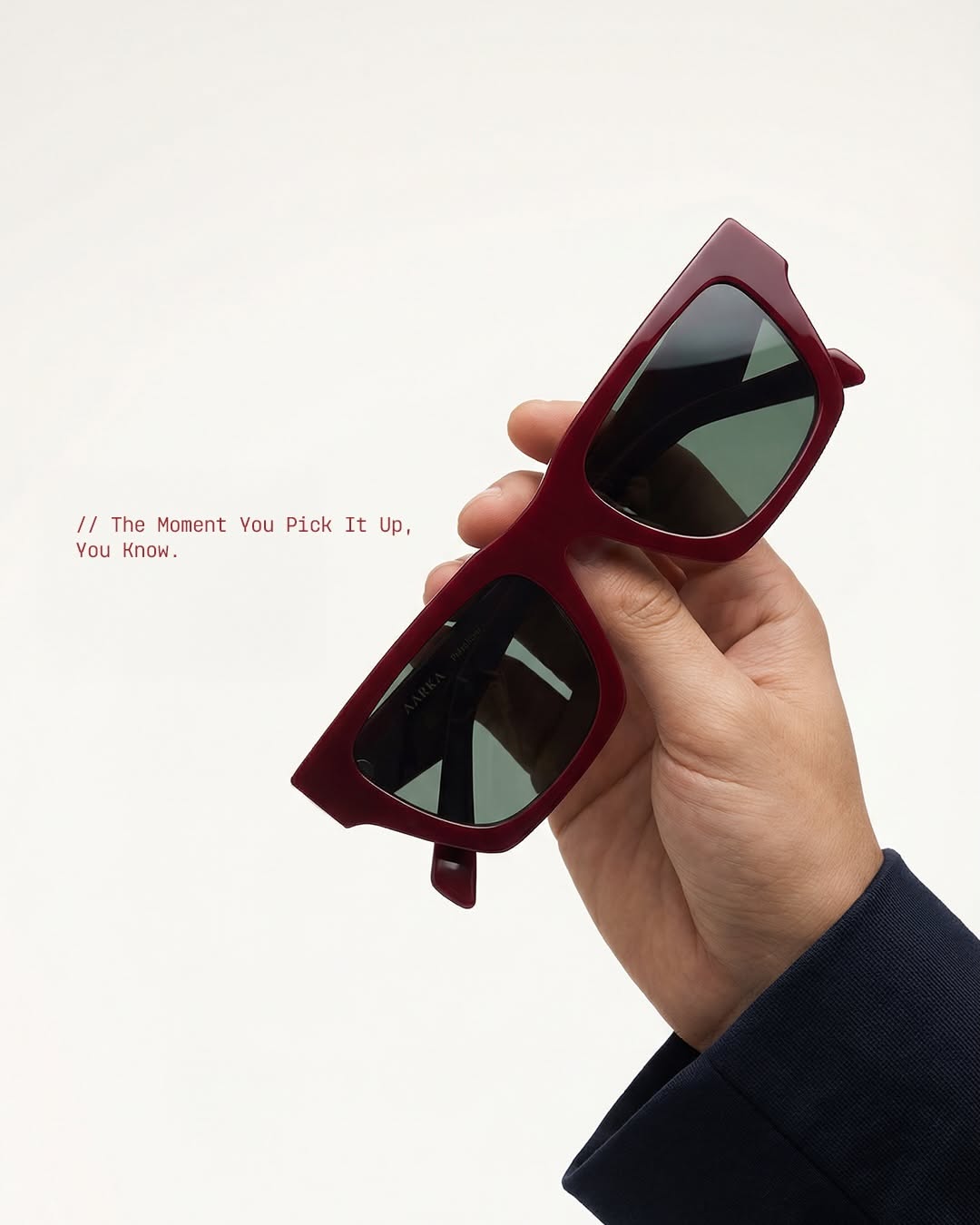 Carousel: Hand resting red acetate sunglasses on a knee in black trousers, slide 2