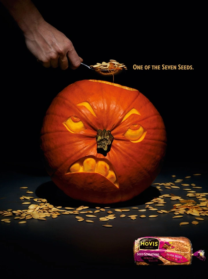 Halloween creative ad: Angry carved pumpkin as a hand scoops out its seeds
