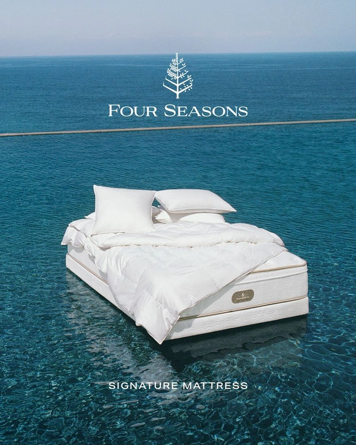 Mattress & Bedding creative ad: Made-up mattress with duvet and pillows floating on an infinity pool facing the sea
