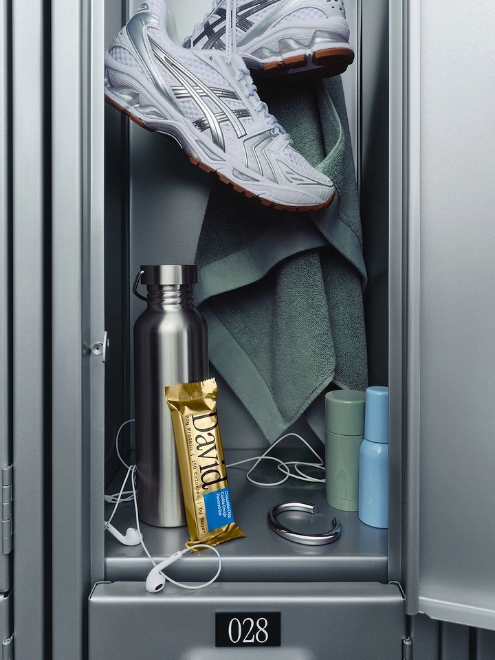Creative ad: Gold protein bar wrapper leaning on a steel bottle inside a gym locker