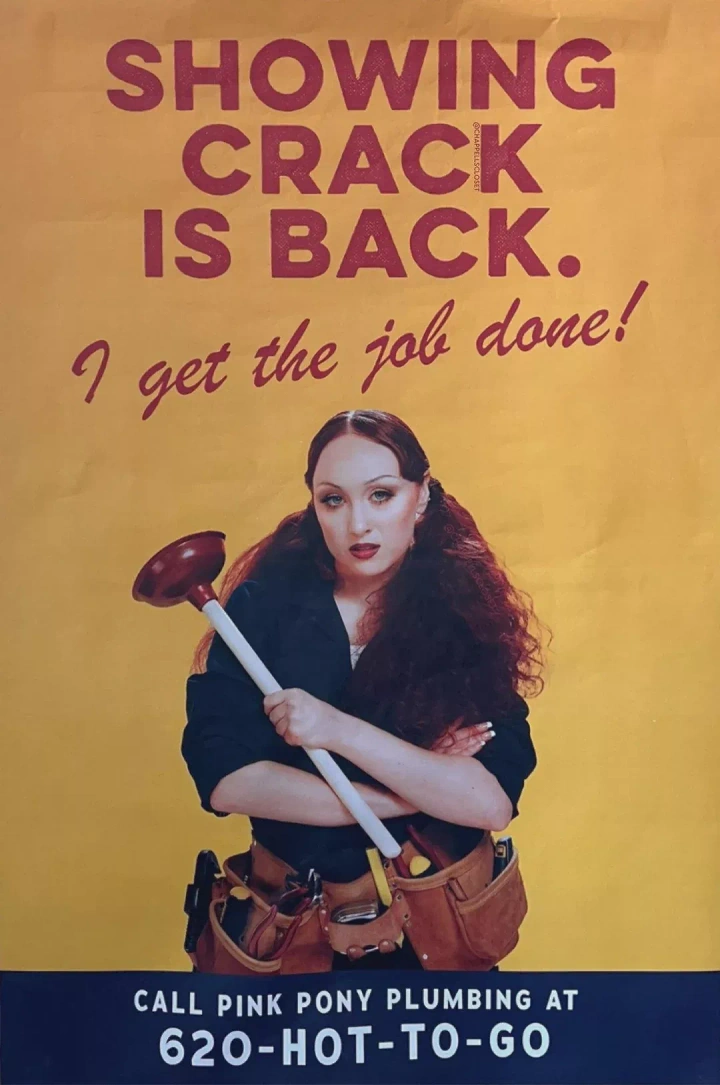 Plumbers creative ad: Red-haired woman in a work shirt and tool belt holding a plunger with arms crossed