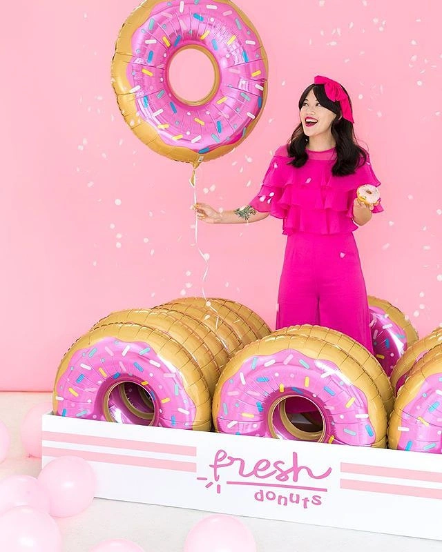 Balloon & Party Decorators creative ad: Woman in pink holding a giant donut balloon beside an oversized donut box