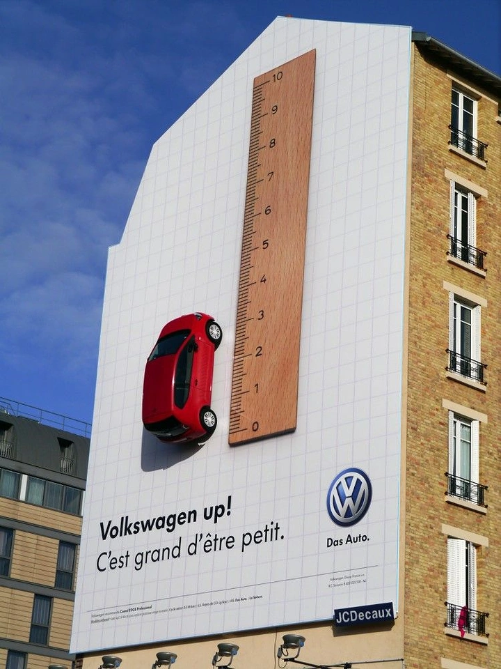 Automotive creative ad: Life-size red city car mounted beside a giant ruler on a building wall