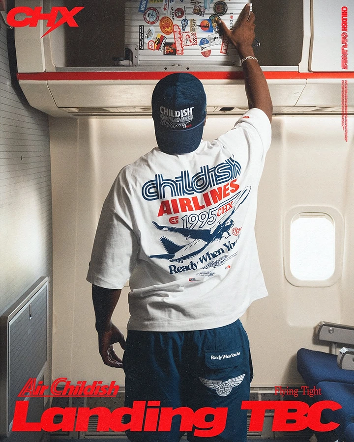 Creative ad: Back view of a model in an airline-themed graphic tee reaching into an aircraft overhead bin