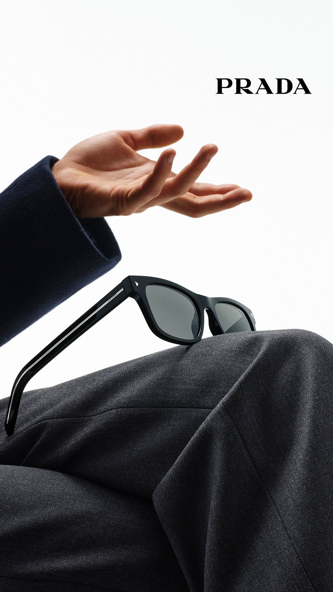 Story: Black sunglasses resting on a suited knee beneath an open hand