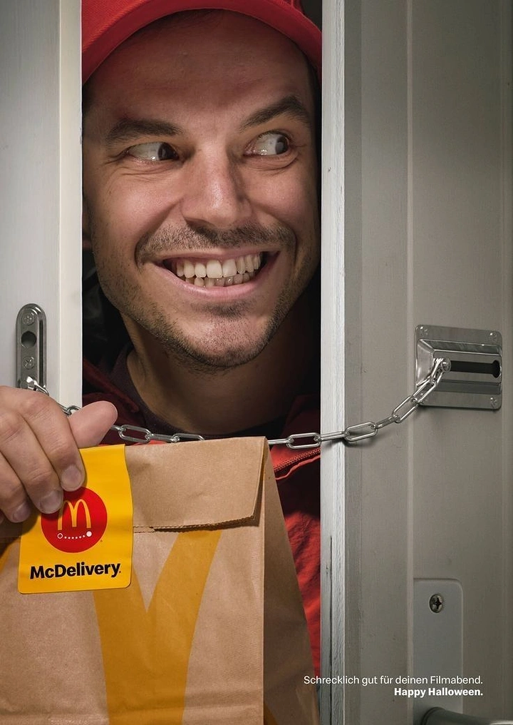 Halloween creative ad: Grinning delivery man peering through a chained door holding a takeaway bag