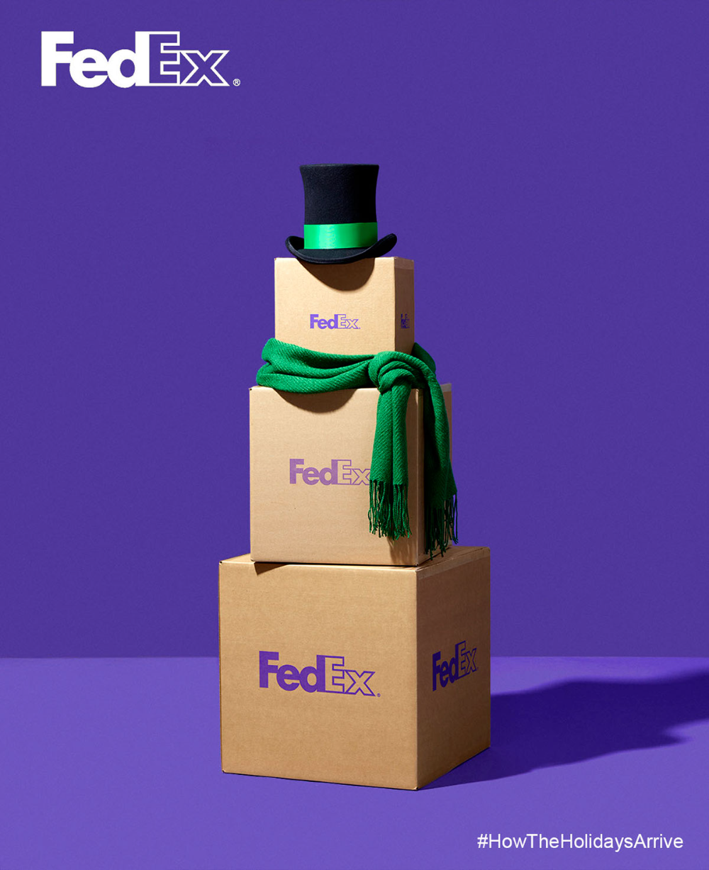 Three stacked shipping boxes dressed as a snowman with a top hat and green scarf