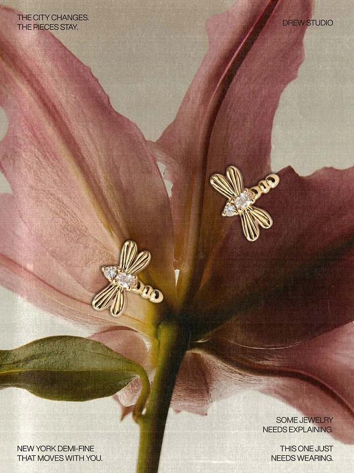 Creative ad: Gold dragonfly stud earrings resting on a pink lily