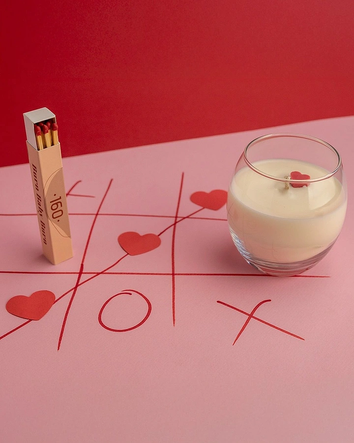 Valentine's Day creative ad: Scented candle and matchbox on a hand-drawn tic-tac-toe with hearts