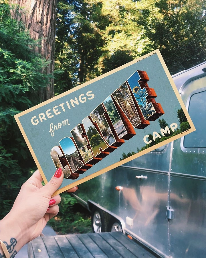 Summer Camps & Kids Activities creative ad: Hand holding a vintage 'Greetings from' large-letter postcard in front of a forest and an Airstream trailer