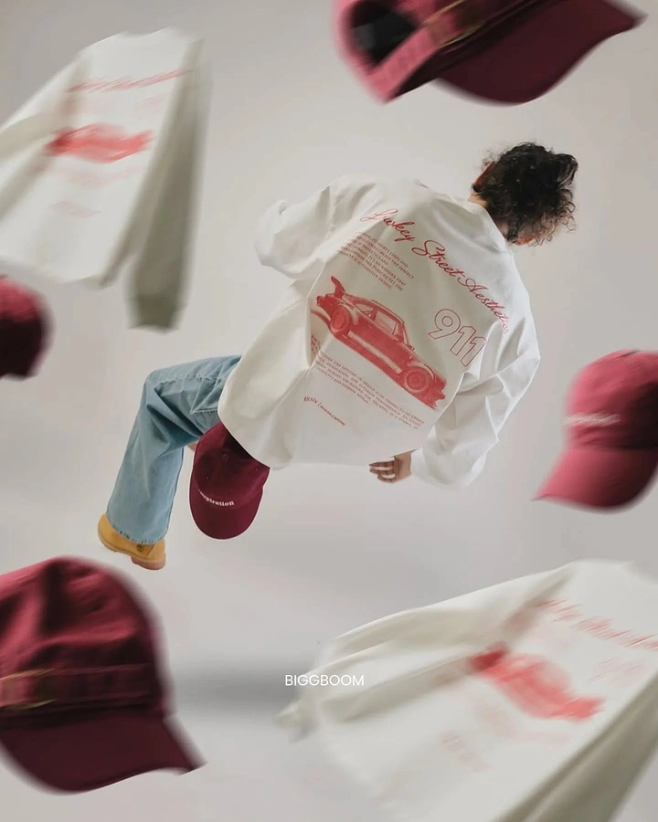 Print-on-Demand & Merch creative ad: Mid-air model in white car-print tee surrounded by flying burgundy caps and tees