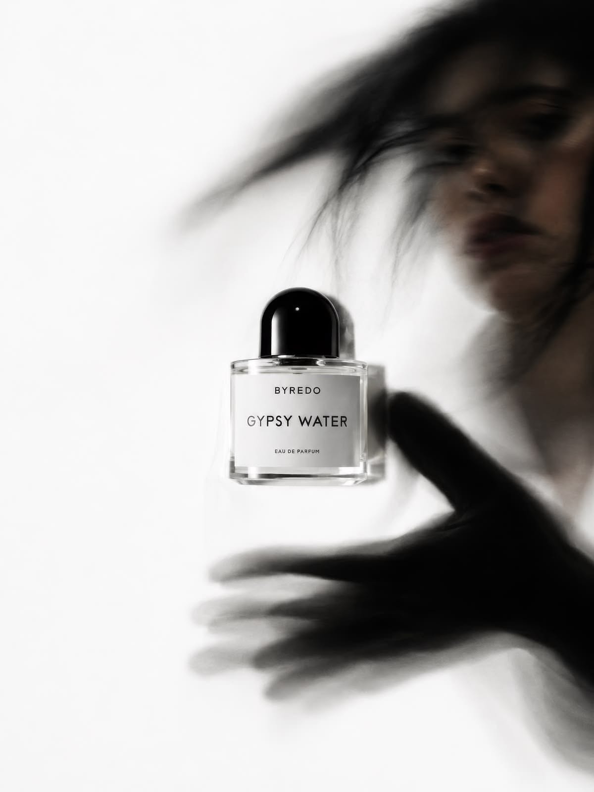 Instagram post: Sharp perfume bottle floating before a motion-blurred woman and hand