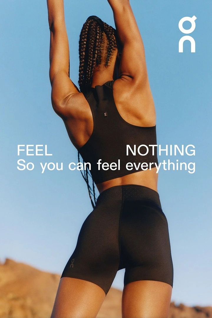 Creative ad: Woman in black sports bra and shorts stretching arms up against the sky, seen from behind