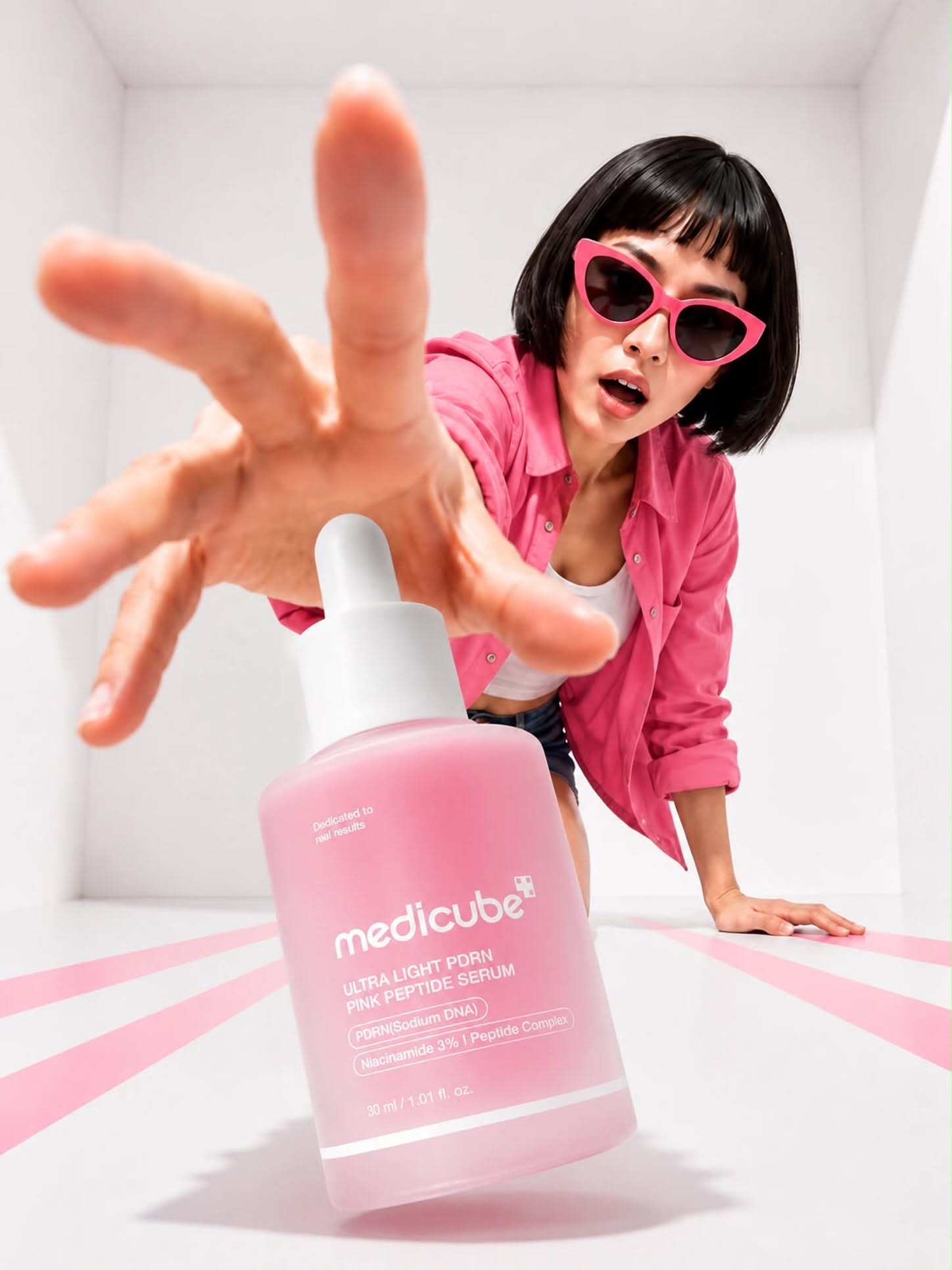 Woman in pink shirt and cat-eye sunglasses lunging to grab a tilted pink serum bottle