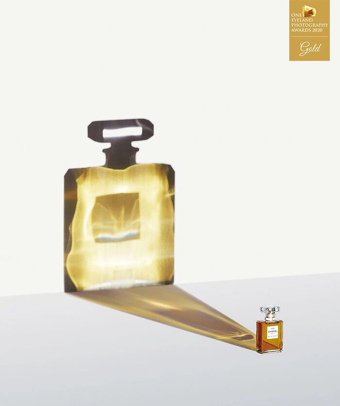 Perfume & Fragrance creative ad: Tiny perfume bottle casting a huge glowing golden shadow on the wall