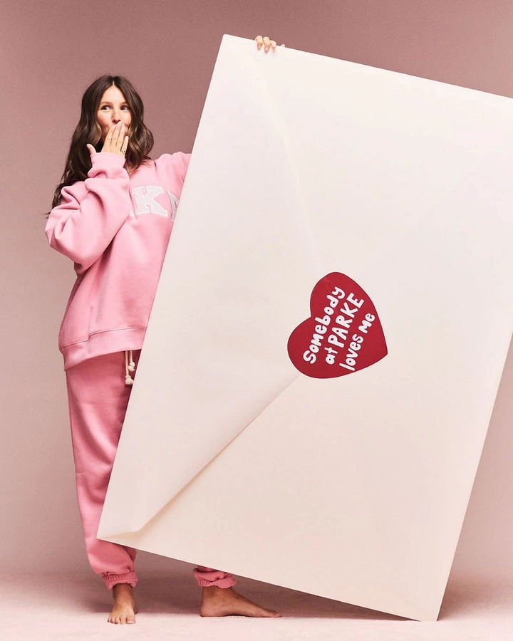 Valentine's Day creative ad: Model in pink sweatsuit holding a giant envelope