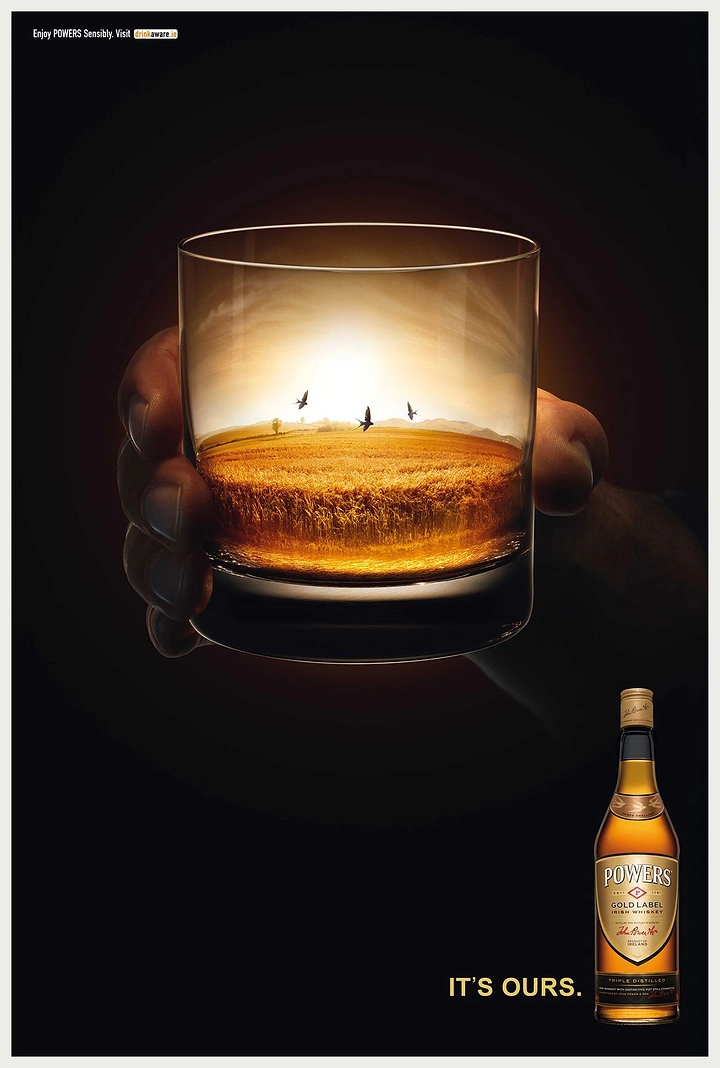 Creative ad: Hand holding a glass whose whiskey becomes a golden barley field at sunset