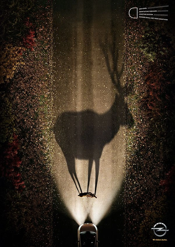 Automotive creative ad: Top-down night road where car headlights cast a giant deer shadow from a tiny deer