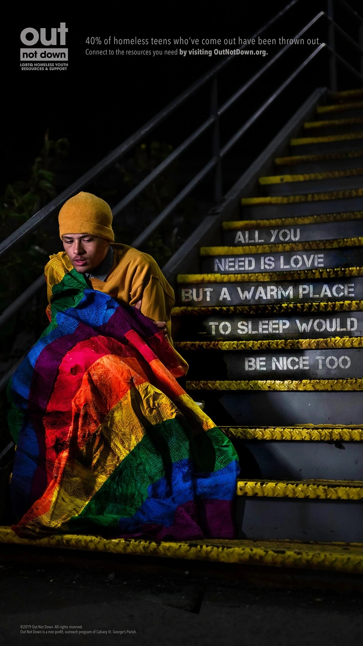 Creative ad: Young man wrapped in a rainbow blanket sitting on night outdoor stairs