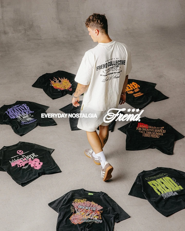 Print-on-Demand & Merch creative ad: Model in a cream tee walking through black graphic tees spread on a grey floor