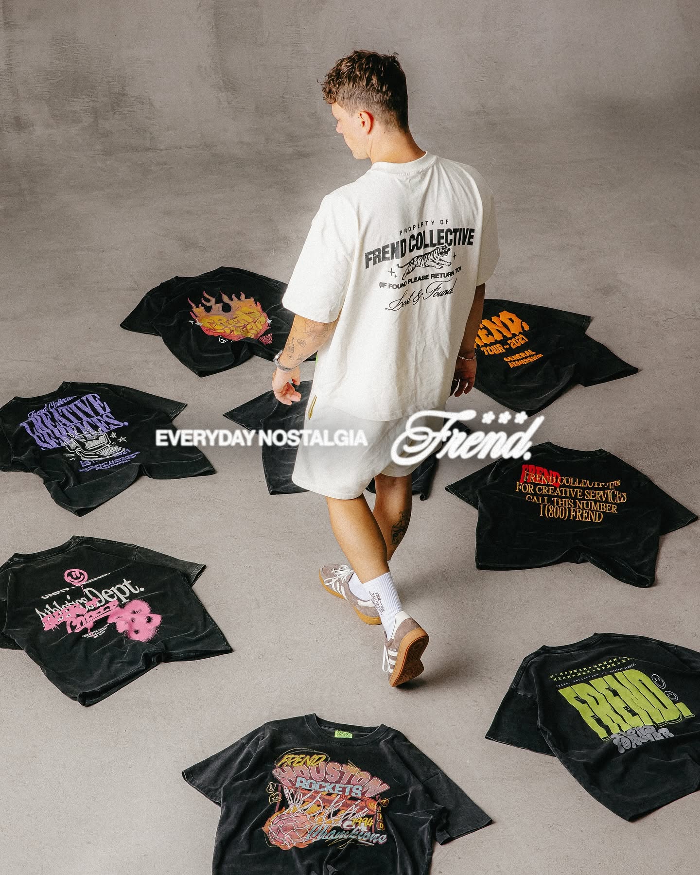 Instagram post: Model in a cream tee walking through black graphic tees spread on a grey floor