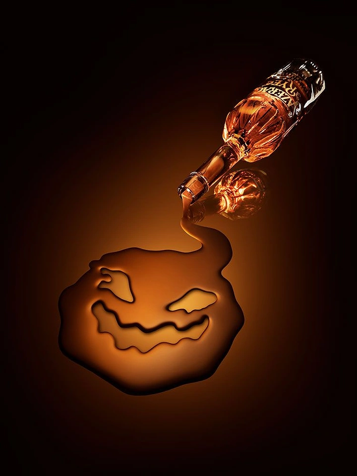 Halloween creative ad: Whisky poured from a bottle into a jack-o'-lantern-face puddle